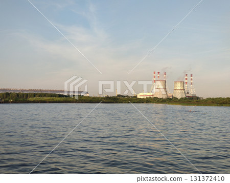 Modern thermal power plant towers on the shore of the Gulf of Finland. The industrial towers emit steam, with a backdrop of greenery, water, and a clear sky. Modern thermal power plant towers on the shore of the Gulf of Finland. The industrial towers emit steam, with a backdrop of greenery, water, and a clear sky. 131372410
