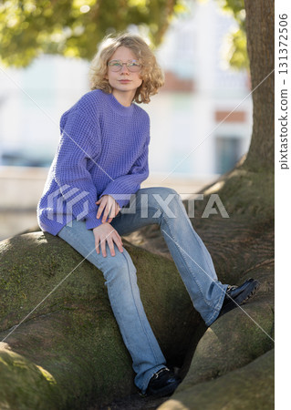 Young woman sitting on tree roots in urban park Young woman sitting on tree roots in urban park 131372506