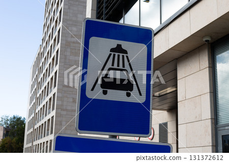 Road sign indicating car wash service, featuring simple icon of a car under water sprays. Set against an urban backdrop, perfect for transport and vehicle service related content 131372612