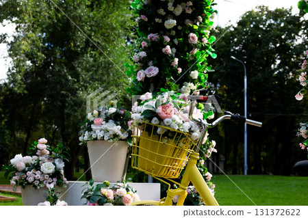 Charming yellow bicycle with a basket full of soft, romantic flowers, creating a serene and stylish outdoor scene. The natural light and greenery highlight the beauty and elegance of the moment 131372622