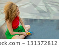 a fashionable woman in bright clothes with long blond curly hair is sitting in the lotus position on the street basking in the sun and resting 131372812