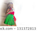 Coquettish s young female model in fashionable elegant bright multicolored green and red clothes looks at her phone against the background of the columns of an office building in the city 131372813