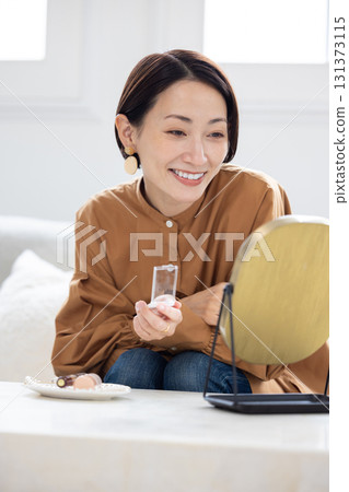 A woman applying skin care lotion in the living room at home 131373115