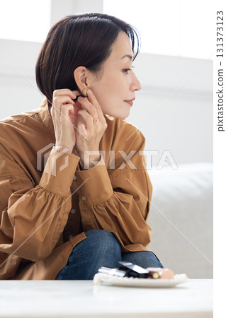 Woman putting on earrings in the living room Woman putting on earrings in the living room 131373123