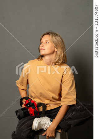Young woman Norwegian photographer with blonde hair sits comfortably on stool, holding a camera and looking thoughtfully towards the side. Woman photographer, artist, mother, creative person portrait Young woman Norwegian photographer with blonde hair sits comfortably on stool, holding a camera and looking thoughtfully towards the side. Woman photographer, artist, mother, creative person portrait 131374607