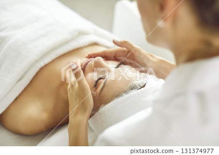 Cosmetologist at beauty and spa salon applies sheet mask on face of relaxed young woman Cosmetologist at beauty and spa salon applies sheet mask on face of relaxed young woman 131374977