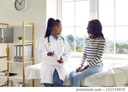Happy African American female doctor and patient talking in examination room at clinic Happy African American female doctor and patient talking in examination room at clinic 131374978