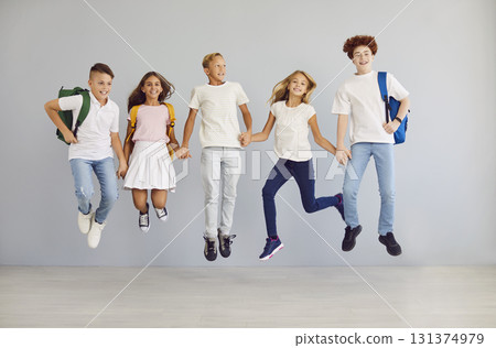 Happy school children looking cheerful at camera, holding hands and jumping together. Happy school children looking cheerful at camera, holding hands and jumping together. 131374979
