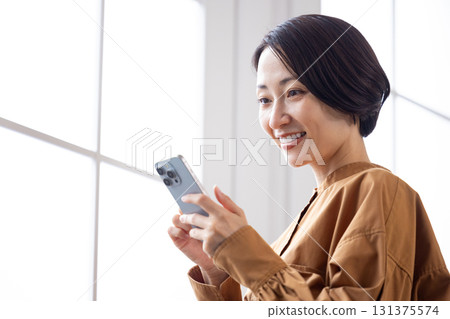A middle-aged woman smiling while looking at her smartphone A middle-aged woman smiling while looking at her smartphone 131375574