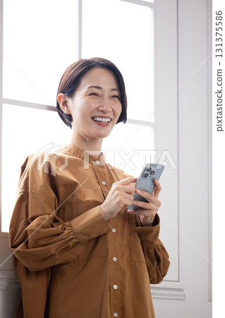 A middle-aged woman smiling while looking at her smartphone 131375586