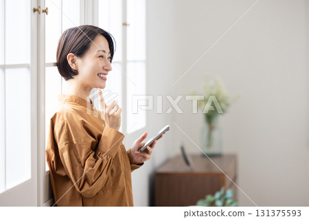 一位中年婦女一邊微笑一邊看著她的智慧型手機 131375593