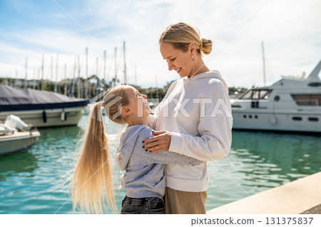 Mother hugging daughter on pier near yachts and calm blue water 131375837