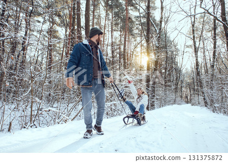 Bearded young man pulling sled with his wife sitting on it Bearded young man pulling sled with his wife sitting on it 131375872