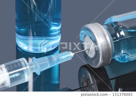 Syringe with a needle stuck in a vial of blue vaccine on dark background 131376081