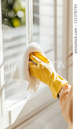Cleaning window with yellow gloves and cloth, sunlight streaming in background, spring cleaning concept, 131376743
