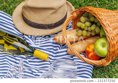 Picnic with wine, fruits, and baguette on a green meadow 131377250