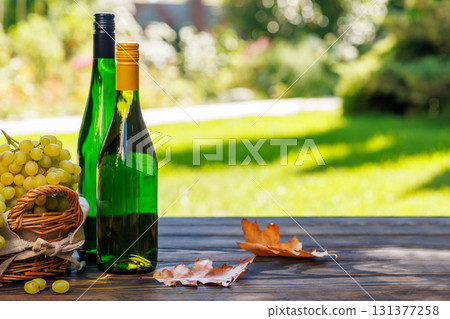 Wine bottles with grapes on a wooden table, glowing with sunny bokeh in the background 131377258