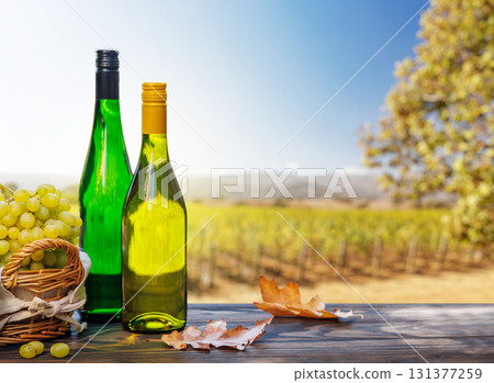 Wine bottles with grapes on a wooden table, glowing with sunny vineyard bokeh in the background Wine bottles with grapes on a wooden table, glowing with sunny vineyard bokeh in the background 131377259