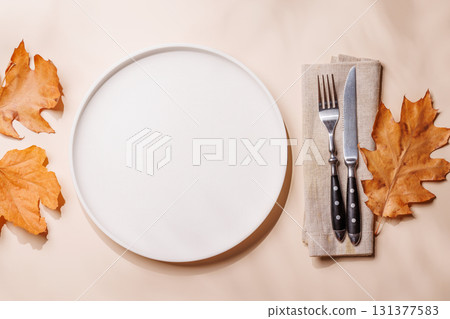Empty plate on beige background surrounded by autumn yellow leaves, seasonal food mockup 131377583