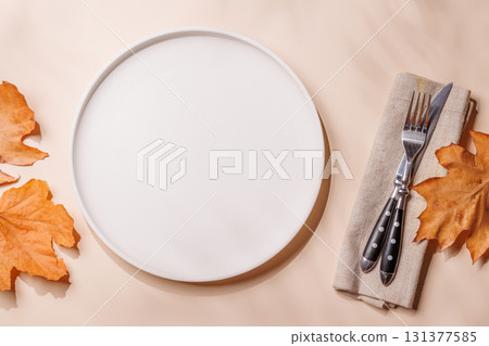 Empty plate on beige background surrounded by autumn yellow leaves, seasonal food mockup 131377585