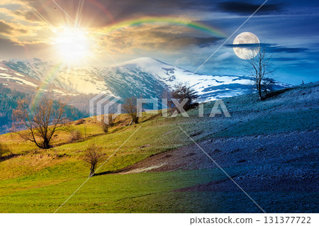 mountainous countryside landscape on spring equinox. day and night time change. grassy field on slope of a hill. mountain ridge with snow capped tops in the distance with sun and moon at twilight 131377722