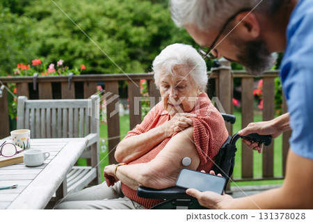 Home nurse checking glucose level of senior lady with smartphone. 131378028