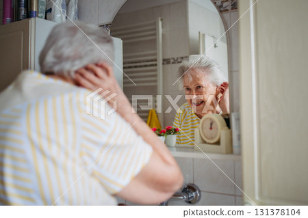 Older woman checking skin and appearance in bathroom. 131378104