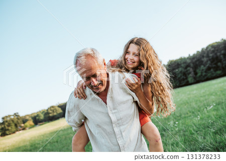 Grandfather playing with granddaughter on meadow. 131378233