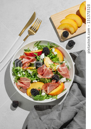 Salad with peaches, arugula, feta, prosciutto and berries in a white plate on a light background Salad with peaches, arugula, feta, prosciutto and berries in a white plate on a light background 131378328