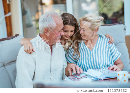 Senior couple showing family photo album to granddaughter. 131378382