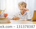 Schoolboy studying at home with a laptop, smiling with a joyful expression 131378387