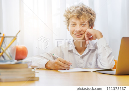 Schoolboy studying at home with a laptop, smiling with a joyful expression 131378387