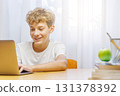Schoolboy studying at home with a laptop, smiling with a joyful expression 131378392