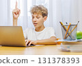 Schoolboy studying at home with laptop, notebook, and learning materials, smiling happily 131378393
