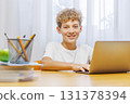 Schoolboy studying at home with laptop, notebook, and learning materials, smiling happily 131378394