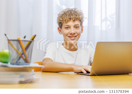 Schoolboy studying at home with laptop, notebook, and learning materials, smiling happily Schoolboy studying at home with laptop, notebook, and learning materials, smiling happily 131378394