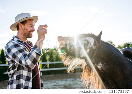 Farmer giving treat to horse on farm. 131378397
