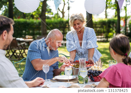 Senior woman serving grilled food during family grill party. Senior woman serving grilled food during family grill party. 131378425