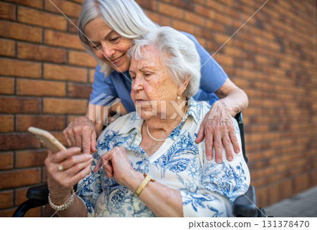 Senior patient in wheelchair showing picture in smartphone to caregiver. 131378470