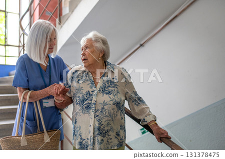 Female healthcare worker helping senior patient walking down the stairs. Female healthcare worker helping senior patient walking down the stairs. 131378475