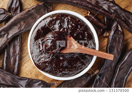 carob cream in a bowl and pods on a wooden table 131378500