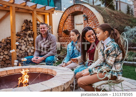 Family roasting marshmallows over open flame, campfire on backyard. 131378505