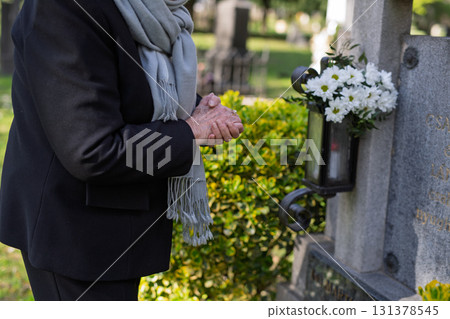 Elderly woman praying at a grave. 131378545