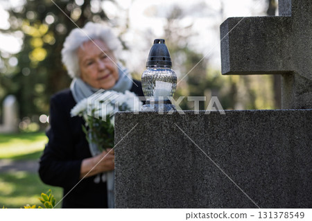 Old woman lighting a candle at a grave. Old woman lighting a candle at a grave. 131378549