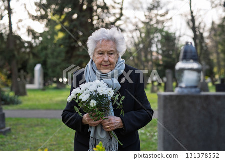 Elderly woman visiting a grave on All Saints Day. Elderly woman visiting a grave on All Saints Day. 131378552