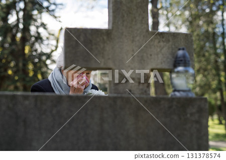 Senior woman crying and mourning at a grave on cemetery. Senior woman crying and mourning at a grave on cemetery. 131378574