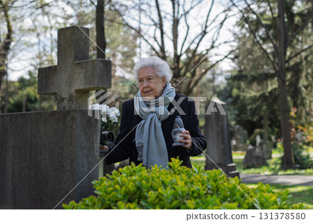 Old woman lighting a candle at a grave. Old woman lighting a candle at a grave. 131378580