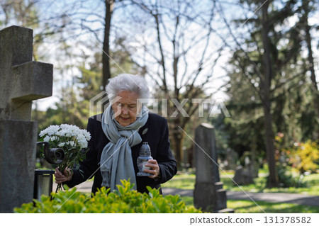 Old woman lighting a candle at a grave. Old woman lighting a candle at a grave. 131378582