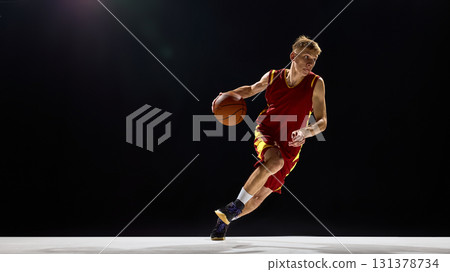Basketball player dribbling with focus and energy on dark background 131378734