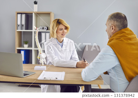 Young woman doctor with medical spine model on desk talking to senior man patient Young woman doctor with medical spine model on desk talking to senior man patient 131378942